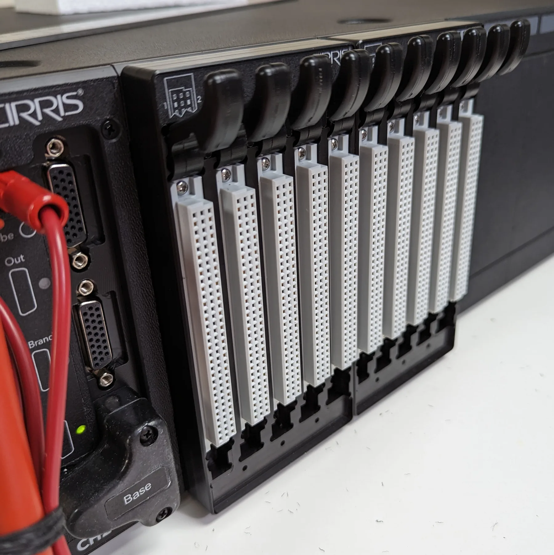 Close-up of a Cirris CH2 cable analyzer, with interface cards, scanner connectors, and red test leads plugged into the base.