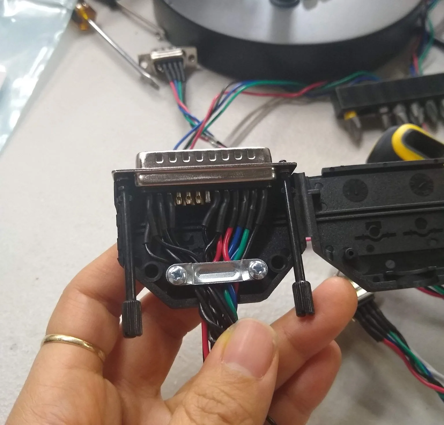 A D-sub connector backshell open during assembly, with color-coded wires clamped inside.