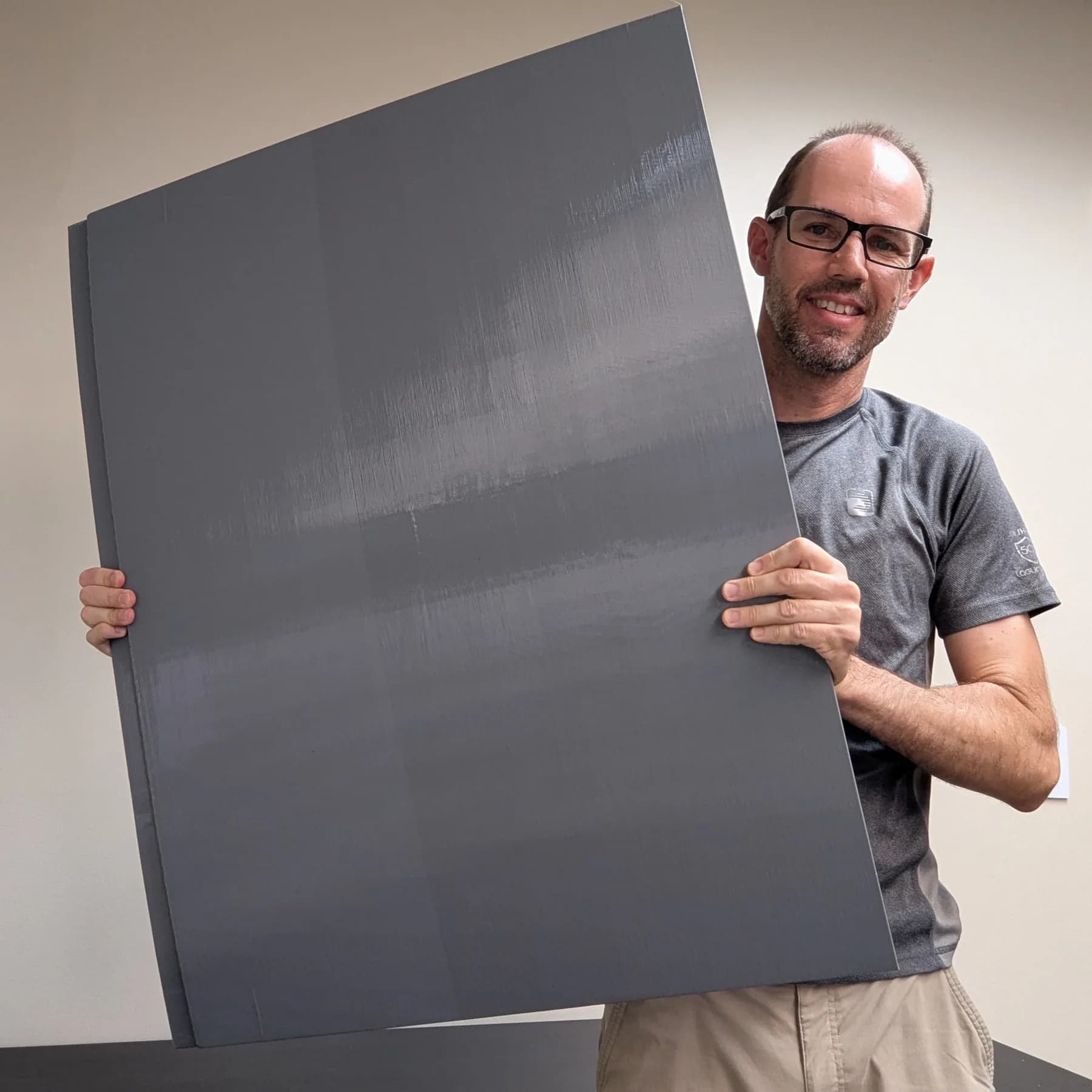 A person holding a large gray 3D-printed panel. The full panel and the person are in frame, so the size of the print is clear.