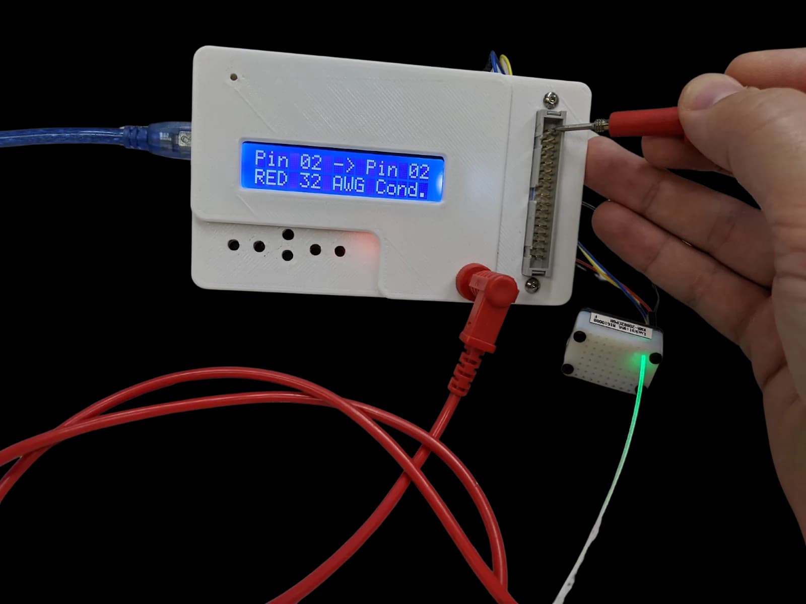 A 3D-printed cable test fixture with an LCD pin readout, a probe on a connector, and a lit fiber lead.
