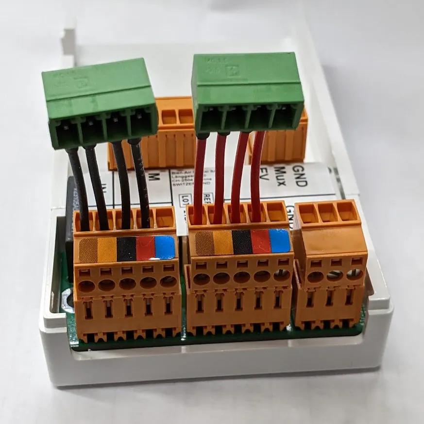 Green terminal blocks mounted in a black enclosure, wired with red and black leads and marked with white labels.